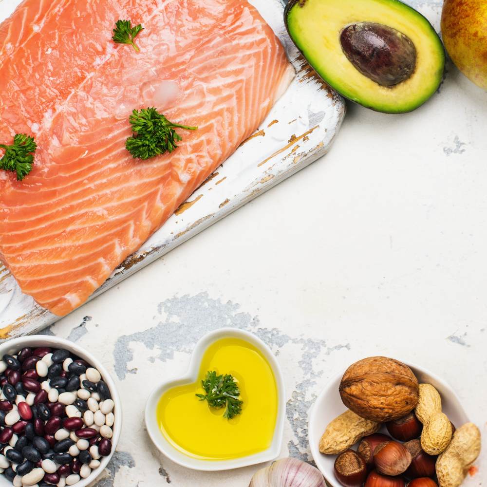 Salmon, avocado sliced in half, butter and various nuts laid on a white surface