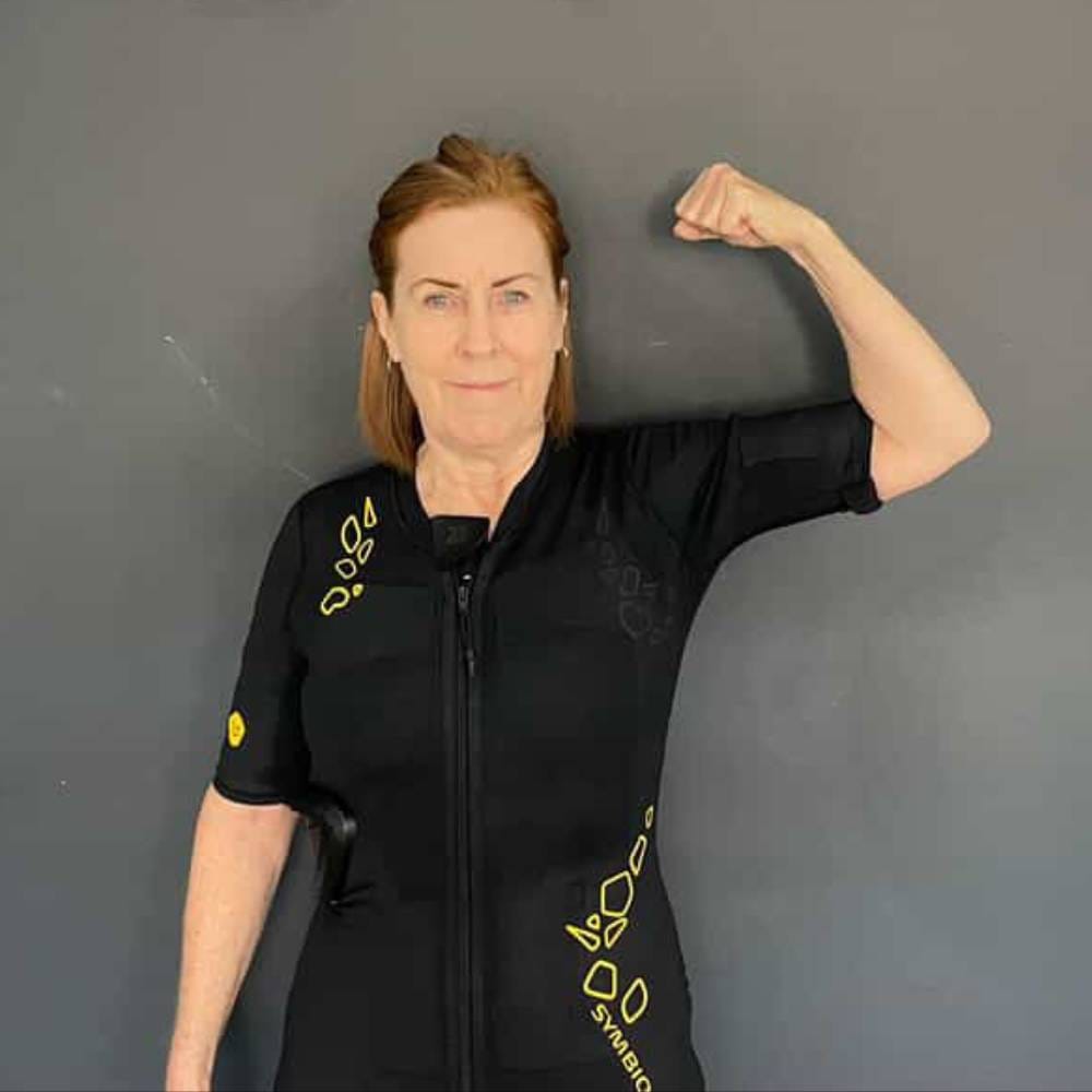 White middle aged woman doing a power pose and smiling in front of a grey wall