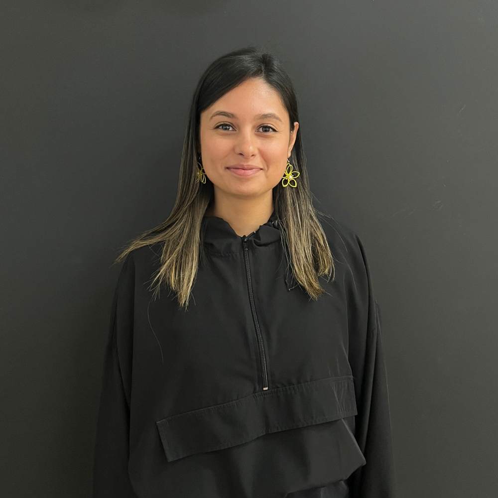 female studio owner standing in front of a grey wall smilling