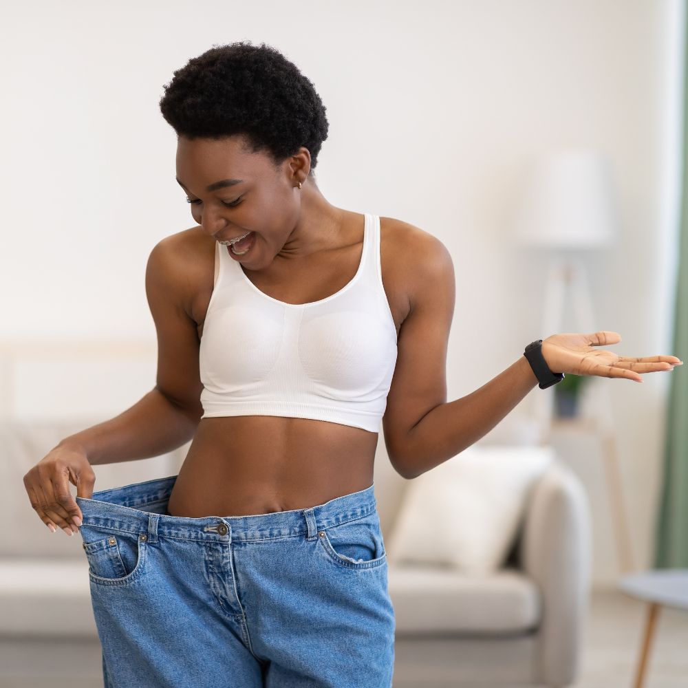 Excited Slim African Woman Wearing Oversized Pants After Weight-Loss Indoor